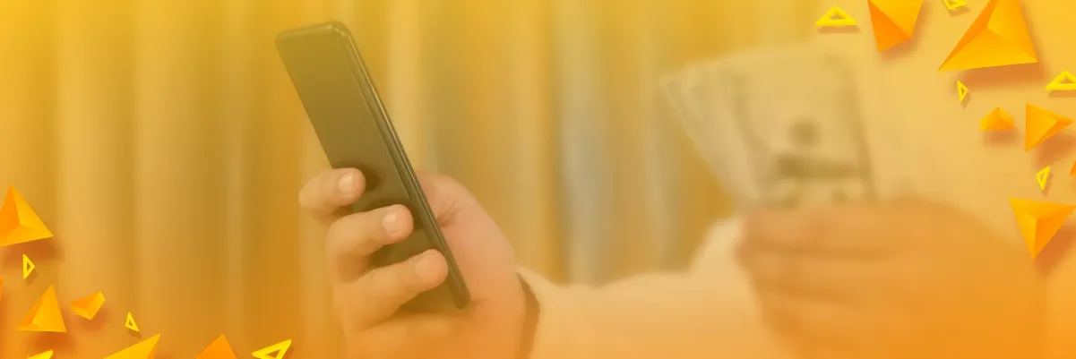 Mano que sostiene un celular junto a billetes